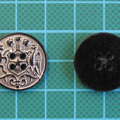 Dois botões, um metálico com brasão e outro preto fosco, sobre base azul em grade