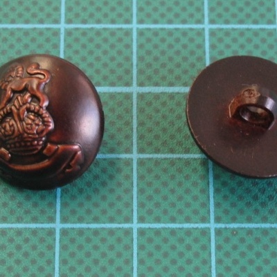 Dois botões metálicos escuros com relevo e argola para coser sobre fundo azul com grelha