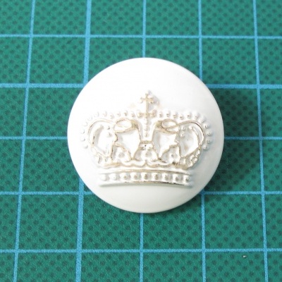 Botão branco com coroa dourada em relevo sobre superfície verde quadriculada