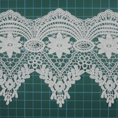 Renda branca com padrão floral sobre superfície verde com grelha quadriculada