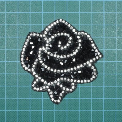 Broche flor preta com pedras pretas e brancas sobre fundo azul quadriculado