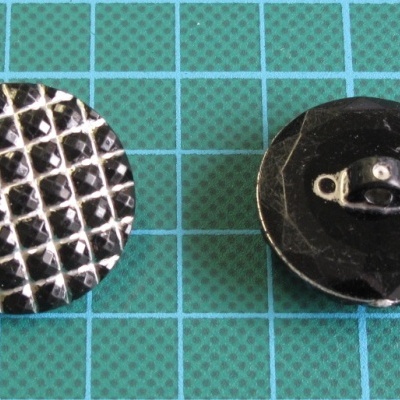 Dois botões redondos pretos, um quadriculado e outro facetado sobre superfície verde quadriculada