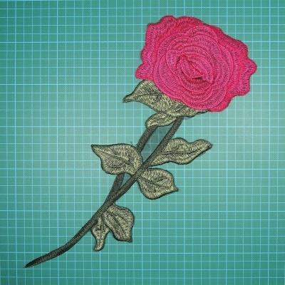 Aplique bordado em forma de rosa cor-de-rosa com caule verde em fundo quadriculado verde