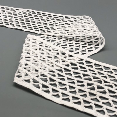 Fita decorativa branca com padrão entrelaçado aberto sobre superfície cinza