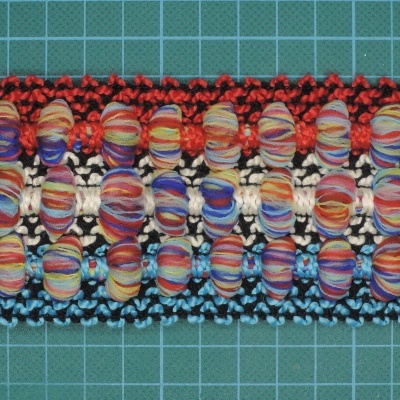 Faixa decorativa colorida trabalhada em tecido sobre superfície quadriculada verde