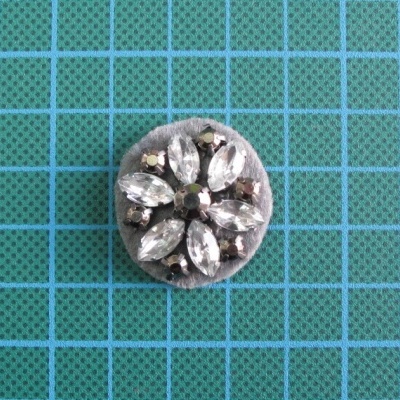 Botão redondo com pedras transparentes facetadas sobre fundo verde com grelha azul