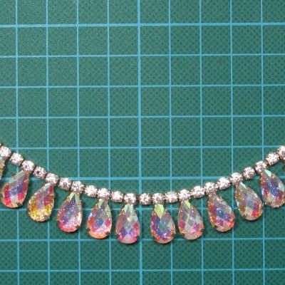 Colar com pedras redondas transparentes e gotas iridescentes sobre fundo de grelha verde