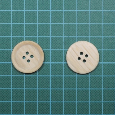 Dois botões redondos de madeira clara com quatro buracos sobre superfície verde quadriculada.