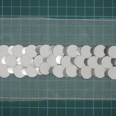 Faixa decorativa de rede cinza com lantejoulas prateadas sobre superfície verde quadriculada