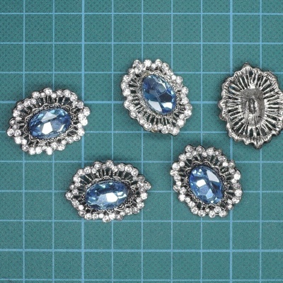 Cinco botões ovais prateados com pedras azuis sobre superfície quadriculada azul