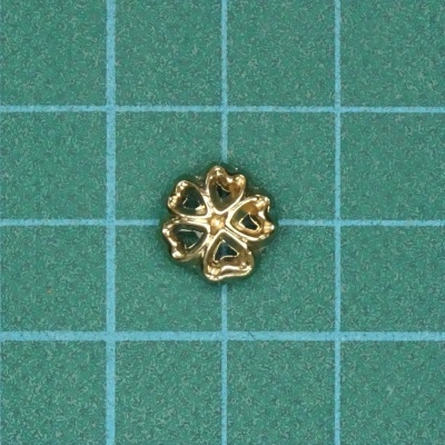 Adorno dourado em forma de flor com pétalas em coração sobre fundo quadriculado verde