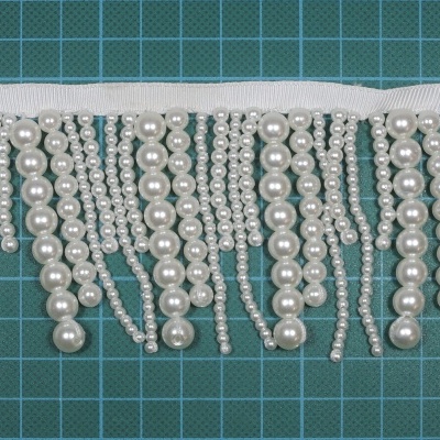 Franja decorativa de pérolas e contas sobre fundo verde quadriculado