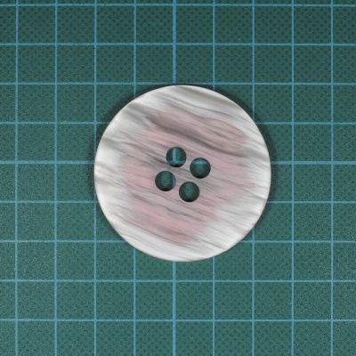 Botão plástico redondo branco com padrão marmorizado rosa e cinza sobre base quadriculada verde.