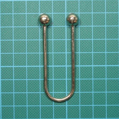 Utensílio metálico em forma de U com bolas nas extremidades sobre superfície quadriculada