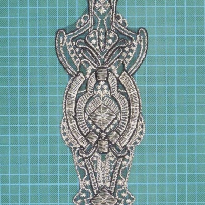 Aplicação bordada cinza e preta com motivos geométricos e florais sobre base azul quadriculada