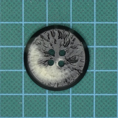 Botão redondo cinza e preto com quatro furos sobre fundo verde com grade azul