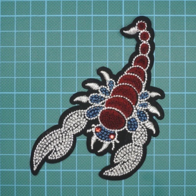 Aplicação bordada de escorpião colorido sobre fundo quadriculado azul