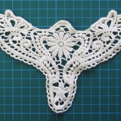 Apliquê de renda branca com padrão floral sobre superfície verde de corte com grelha