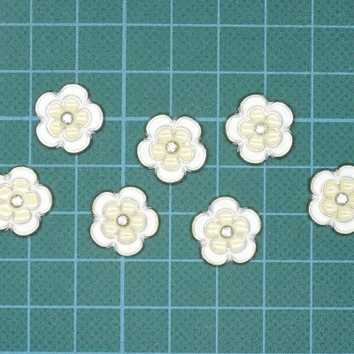 Sete botões florais bege claro sobre superfície verde com grelha branca