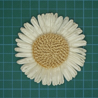 Flor decorativa branca com centro trançado bege sobre superfície verde quadriculada