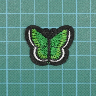 Patch bordado em forma de borboleta verde sobre fundo em grade azul esverdeada