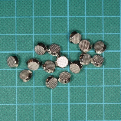 Pequenos objetos redondos metálicos sobre base verde com grelha azul