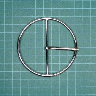 Fivela circular metálica prateada com design de três barras sobre fundo verde quadriculado