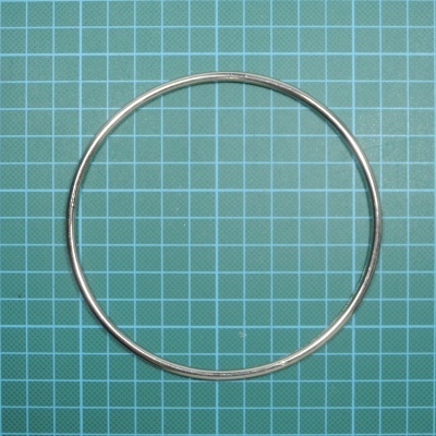 Anel metálico prateado sobre superfície quadriculada azul-esverdeada