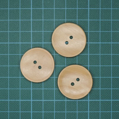 Três botões redondos bege com dois orifícios em superfície verde quadriculada