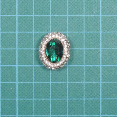 Anel com pedra verde oval rodeada de cristais sobre fundo quadriculado azul