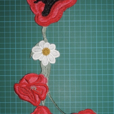 Apliques de tecido bordado de flores vermelhas e branca sobre base com grade verde.