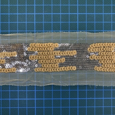 Fita decorativa com lantejoulas douradas e prateadas sobre rede transparente