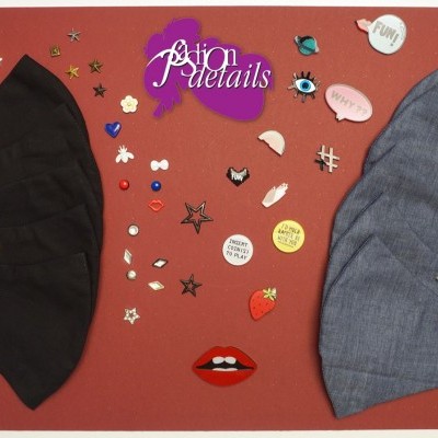 Máscaras pretas e cinzentas com pins decorativos coloridos sobre fundo vermelho com logótipo