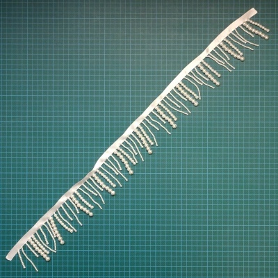 Franja decorativa branca com contas sobre fundo verde quadriculado