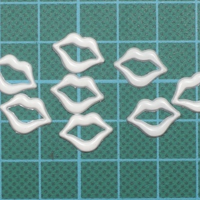 Oitos moldes brancos em forma de lábios sobre tapete de corte verde com grelha azul