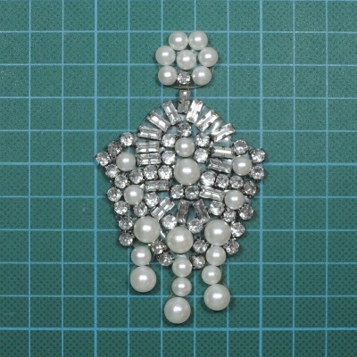 Pendente de bijuteria com pérolas e pedras brilhantes em fundo quadriculado