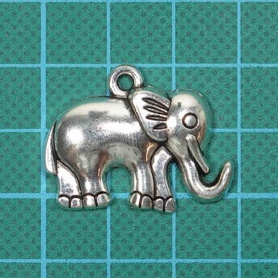 Pingente metálico de elefante prateado sobre superfície verde quadriculada
