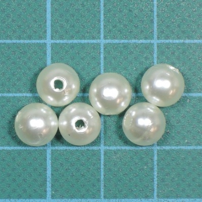 Seis contas de imitação de pérola brancas sobre base quadriculada azul claro