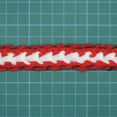 Fita têxtil entrelaçada vermelha e branca sobre fundo verde quadriculado