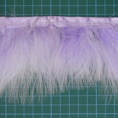 Franja de penas branco e lilás com base de tecido sobre superfície verde quadriculada