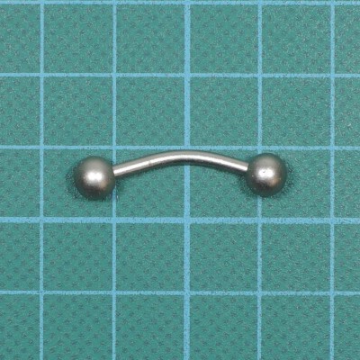 Piercing curvo metálico com esferas em fundo verde quadriculado