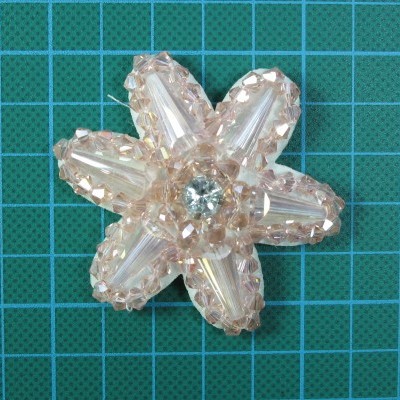 Flor decorativa de contas de vidro cor de rosa com pedra azul no centro sobre superfície quadriculada azul