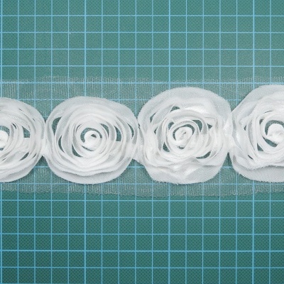 Faixa decorativa branca de tecido rendado com flores em forma de rosetas sobre base de grade verde