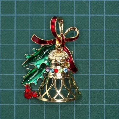 Broche de sino dourado com laço vermelho e folhas verdes sobre fundo de grade verde
