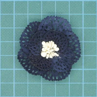 Flor de crochet azul escuro com pistilos brancos sobre superfície verde quadriculada