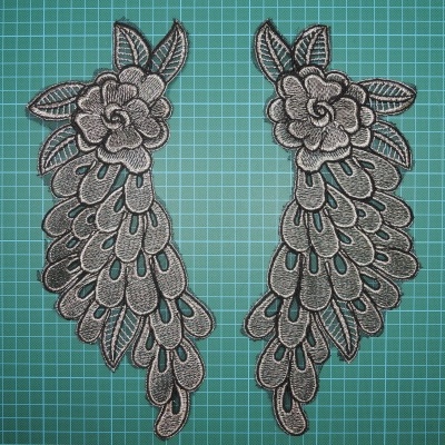 Par de aplicações bordadas com padrão floral cinzentas sobre fundo verde quadriculado.