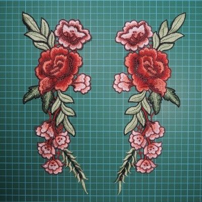  Dois bordados floridos com rosas vermelhas e folhas verdes sobre fundo verde com grade.