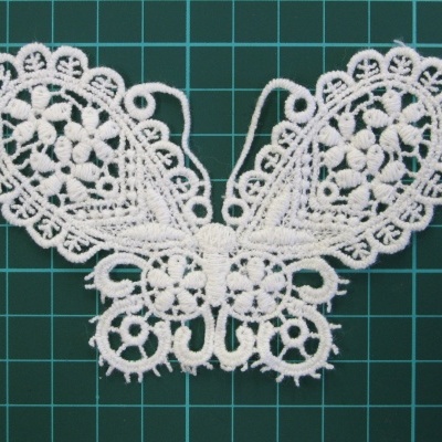 Aplicação têxtil branca em forma de borboleta em renda sobre superfície verde quadriculada