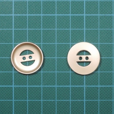 Dois botões redondos bege claro com quatro orifícios sobre fundo verde quadriculado