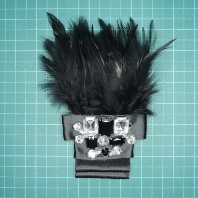 Adorno com plumas pretas, fita preta e cristais decorativos sobre fundo quadriculado verde